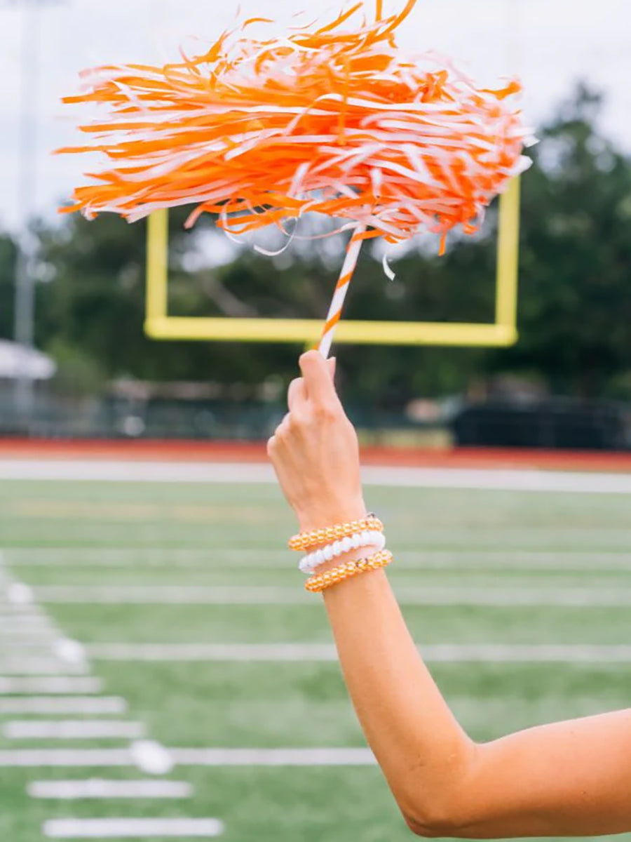 woman shaking orange and white shaker with orange and white pony tail holders on her wrist