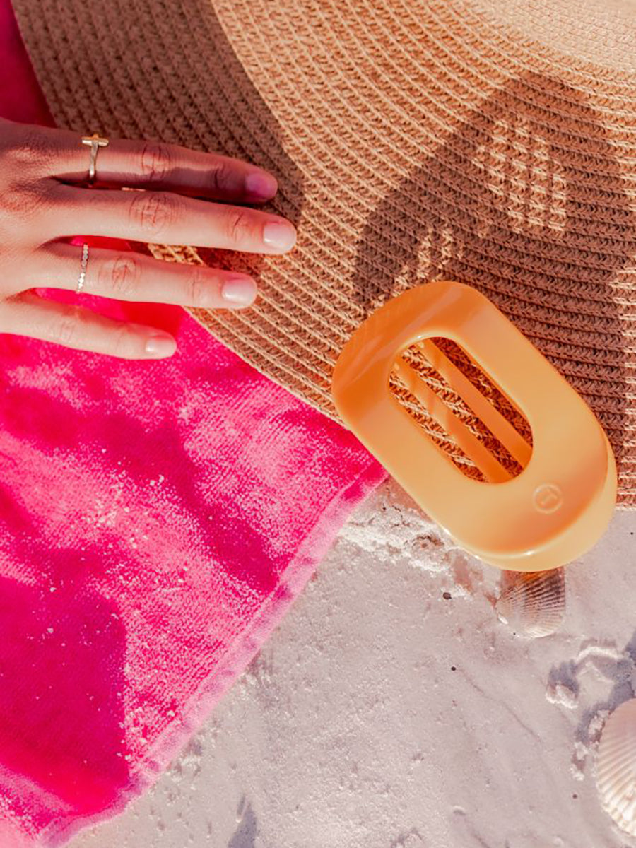 orange hair clip laying with a woman's hat in the sand